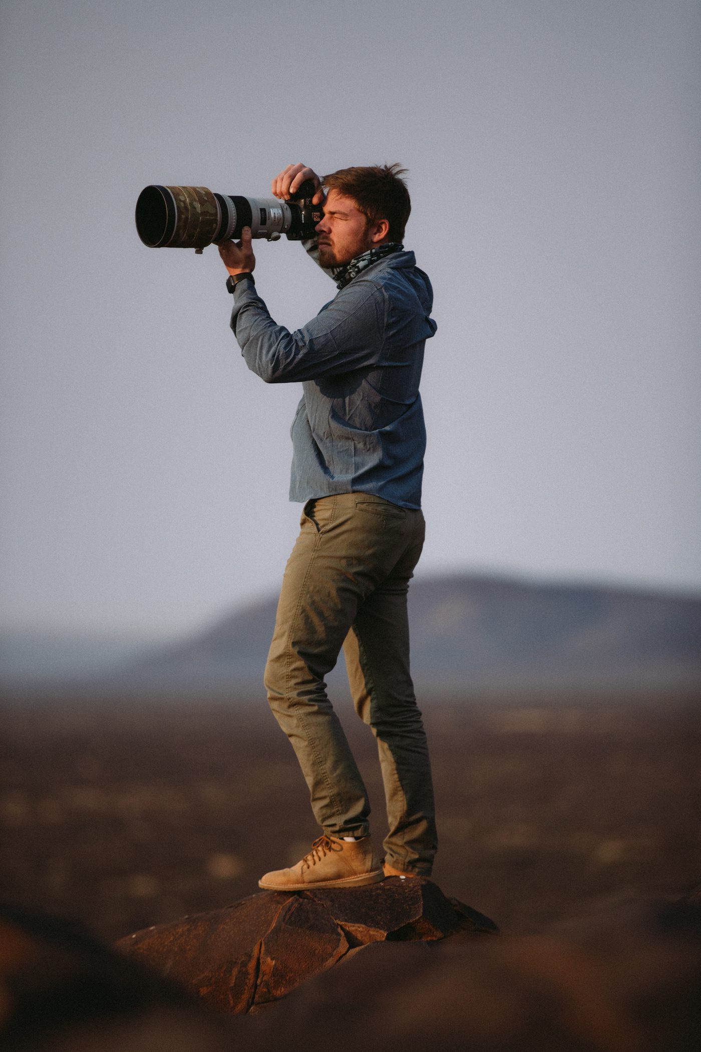 Jacques standing on a rock, photographing with a long lens, hills in the haze behind him